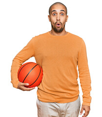 Wall Mural - Hispanic adult man holding basketball ball scared and amazed with open mouth for surprise, disbelief face