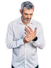 Poster - Middle age hispanic with grey hair wearing casual white shirt suffering pain on hands and fingers, arthritis inflammation