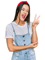 Poster - Young hispanic girl wearing casual clothes smiling with happy face winking at the camera doing victory sign. number two.