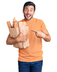 Wall Mural - Young hispanic man holding paper bag with bread smiling happy pointing with hand and finger