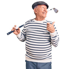 Sticker - Senior handsome grey-haired man holding golf club and ball pointing thumb up to the side smiling happy with open mouth