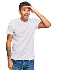 Wall Mural - Young handsome african american man wearing casual white tshirt very happy and smiling looking far away with hand over head. searching concept.