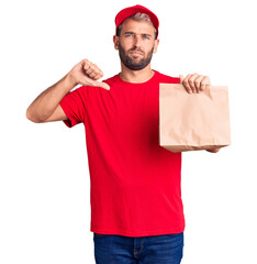 Poster - Young handsome blond man holding delivery paper bag with angry face, negative sign showing dislike with thumbs down, rejection concept