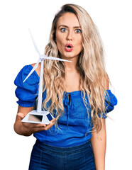 Poster - Young blonde woman holding solar windmill for renewable electricity scared and amazed with open mouth for surprise, disbelief face