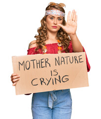 Sticker - Young blonde girl wearing hippie style holding mother nature is crying protest cardboard banner with open hand doing stop sign with serious and confident expression, defense gesture