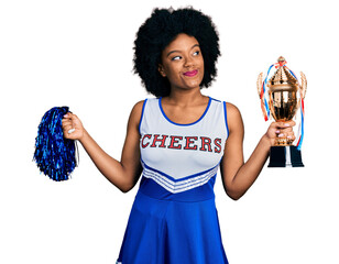 Canvas Print - Young african american woman wearing cheerleader uniform holding pompom and trophy smiling looking to the side and staring away thinking.