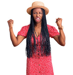 Wall Mural - Young african american woman wearing summer hat angry and mad raising fists frustrated and furious while shouting with anger. rage and aggressive concept.