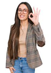 Wall Mural - Young hispanic girl wearing business clothes and glasses smiling positive doing ok sign with hand and fingers. successful expression.