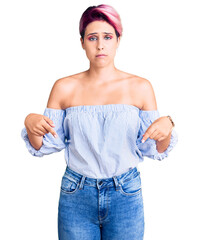 Sticker - Young beautiful woman with pink hair wearing casual clothes pointing down looking sad and upset, indicating direction with fingers, unhappy and depressed.