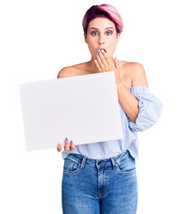 Canvas Print - Young beautiful woman with pink hair holding cardboard banner with blank space covering mouth with hand, shocked and afraid for mistake. surprised expression