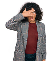 Poster - Young hispanic woman wearing business clothes peeking in shock covering face and eyes with hand, looking through fingers with embarrassed expression.