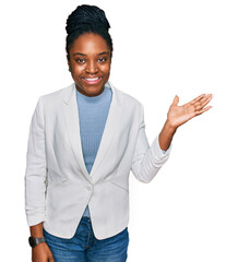 Canvas Print - Young african american woman wearing business clothes smiling cheerful presenting and pointing with palm of hand looking at the camera.