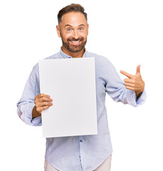 Sticker - Handsome middle age man holding blank empty banner smiling happy pointing with hand and finger