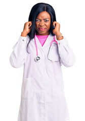 Sticker - Young african american woman wearing doctor stethoscope covering ears with fingers with annoyed expression for the noise of loud music. deaf concept.