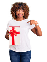 Poster - Young african american woman holding gift pointing finger to one self smiling happy and proud