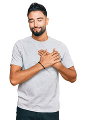 Canvas Print - Young man with beard wearing casual grey tshirt smiling with hands on chest with closed eyes and grateful gesture on face. health concept.