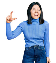 Poster - Young brunette woman with blue eyes doing size gesture holding invisible object smiling and laughing hard out loud because funny crazy joke.