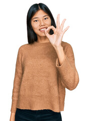 Poster - Beautiful young asian woman wearing casual winter sweater smiling positive doing ok sign with hand and fingers. successful expression.