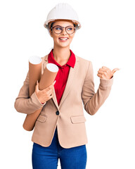 Poster - Young beautiful woman wearing architect hardhat and glasses holding blueprints pointing thumb up to the side smiling happy with open mouth