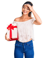 Canvas Print - Young beautiful woman holding gift stressed and frustrated with hand on head, surprised and angry face