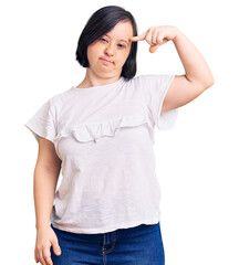 Wall Mural - Brunette woman with down syndrome wearing casual white tshirt pointing unhappy to pimple on forehead, ugly infection of blackhead. acne and skin problem