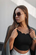 © alones - Beautiful young woman model in fashion urban clothes with sunglasses with blazer standing on the street near a white wall. Pretty elegant girl