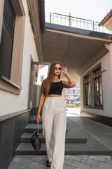Wall Mural - Trendy young beautiful successful business woman in fashion clothes with a stylish bag puts on sunglasses and walks on the street. Pretty girl