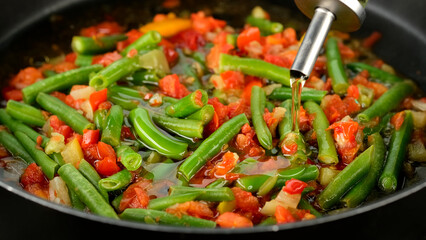 Wall Mural - Pouring oil for frying vegetables in pan. Green beans, tomatoes, bell peppers ready for cooking