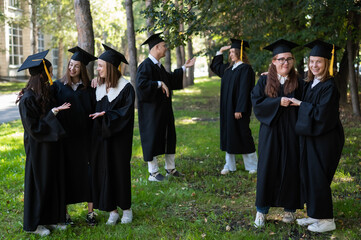 A group of graduates in robes congratulate each other on their graduation outdoors.