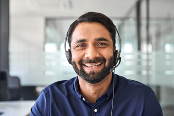 Wall Mural - Male Indian contract service representative telemarketing operator smiling to camera. Happy man call center agent or salesman wearing headset working in customer support office. Close up portrait.