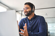 Happy Indian call center agent wearing headset talking to client working in customer support office. Professional contract service telemarketing operator using laptop having conversation. Candid shot