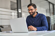 © insta_photos - Happy professional Indian business man company employee, male worker, manager or financial analyst smiling looking at computer satisfied with work results and profit growth sitting at office desk.