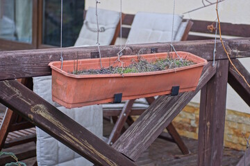 Wall Mural - one brown plastic flowerpot with gray soil hanging on a wooden fence board on the street