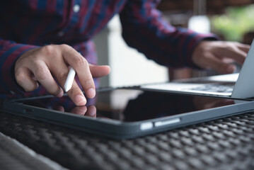 Wall Mural - Casual business man using digital tablet, touching on screen and working on laptop computer, surfing the internet at coffee shop, close up. Man freelancer online working from cafe