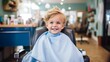 © ND STOCK - A 3-year-old boy wearing a protective cape sits in a happy barber's chair while getting a haircut in a cutely decorated shop for children.
