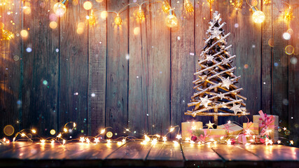 Wall Mural - christmas decoration - wooden tree on table with rustic lights and abstract defocused snowing