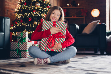 Poster - Portrait of optimistic lovely teenager with blond hair dressed red sweater sitting cuddle gift box at christmas eve in house indoors