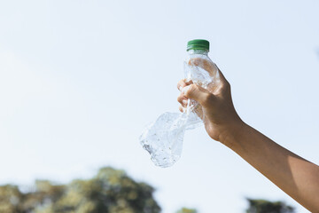  Recyclable plastic bottle held in hand up on sky background. Hand holding plastic waste for recycle reduce and reuse concept to promote clean environment with effective recycling management. Gyre