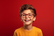 Un enfant heureux et souriant portant des lunettes et un tee-shirt orange, arrière-plan isolé, coloré, rouge.