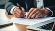 © Studio Nova - Close-up of a businessman signing a report, with a laptop on the desk