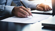 © MP Studio - Close-up of a businessman signing a report, with a laptop on the desk
