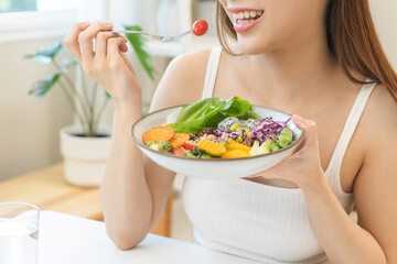 Diet concept, happy asian young woman hand use a fork to prick tomato, fresh vegetable or green salad, eat nutrition food  on table at home, low fat to good body. Girl getting weight loss for healthy.