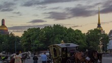Romantic Carriage Rides On Palace Square At Sunset Timelapse In St. Petersburg. Admiralty Building And St. Isaac's Cathedral Grace The Background