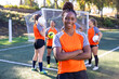 © Mat Hayward - Young African American woman standing with a soccer ball in front of afFemale soccer team. The women players work together as a team in a group of five wearing matching orange jerseys.