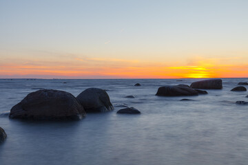 Wall Mural - Sunset over the sea, orange strip of sunshine. Erratic boulders appearing from the water.
