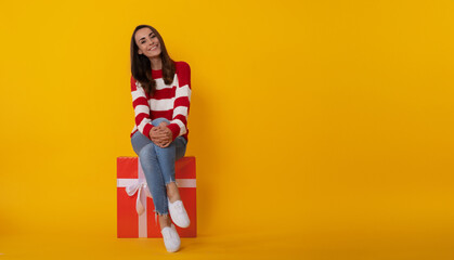 Wall Mural - Photo of an attractive smiling young trendy woman with gift box isolated on yellow background. Birthday, anniversary, holidays, Christmas, St. Valentine's Day