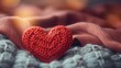 A red knitted heart rests on a cozy grey blanket, symbolizing warmth and love