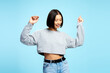 Cheerful Asian woman wearing casual clothes dancing, looking away isolated on blue background