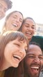 © CarlosBarquero - Happy smiling multi-ethnic group friends having fun together. Multiracial diverse young colleagues embracing posing for selfie photo on street in city. Multicultural friendship generation Z concept.