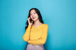 © Parichat - Asian woman poses while talking on the phone while standing in front of a light blue background.